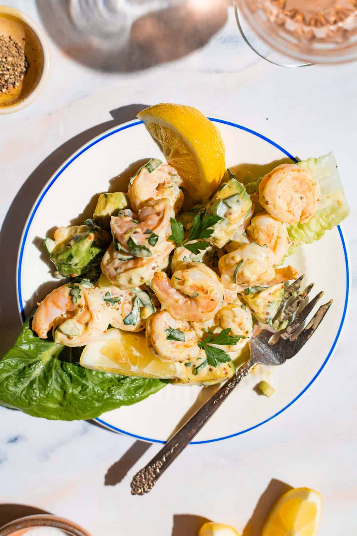 Overhead shot of a serving of shrimp salad on a plate with a lemon wedge on the side.