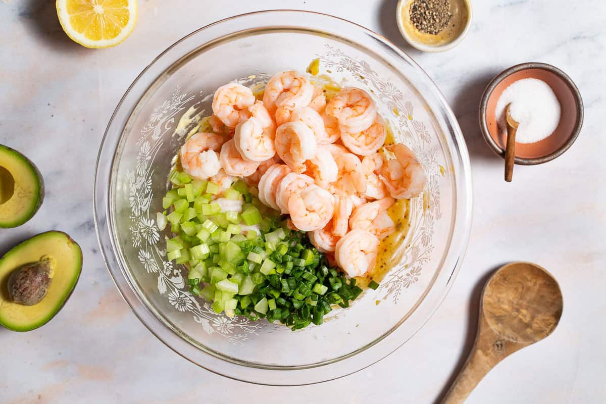 glass bowl with dressing, shrimp, celery, and green onions before being mixed.