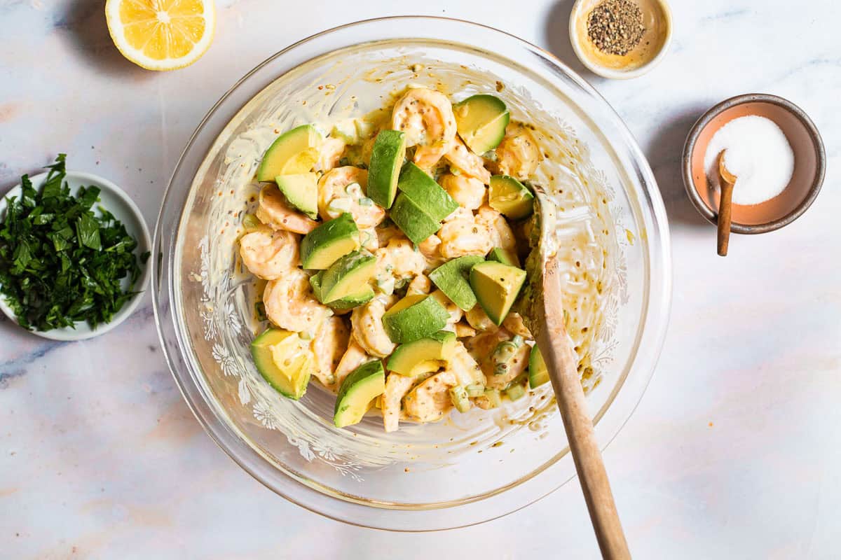 avocado being added to shrimp salad.