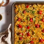 Baked hash browns on a sheet pan surrounded by a kitchen towel and bowls of salt and pepper.