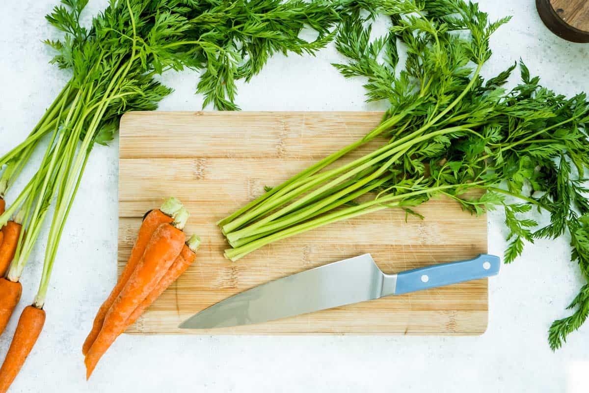 An overhead photo of carrots just separated from their tops on a cutting board with a knife. Next to this is a bunch of carrots.