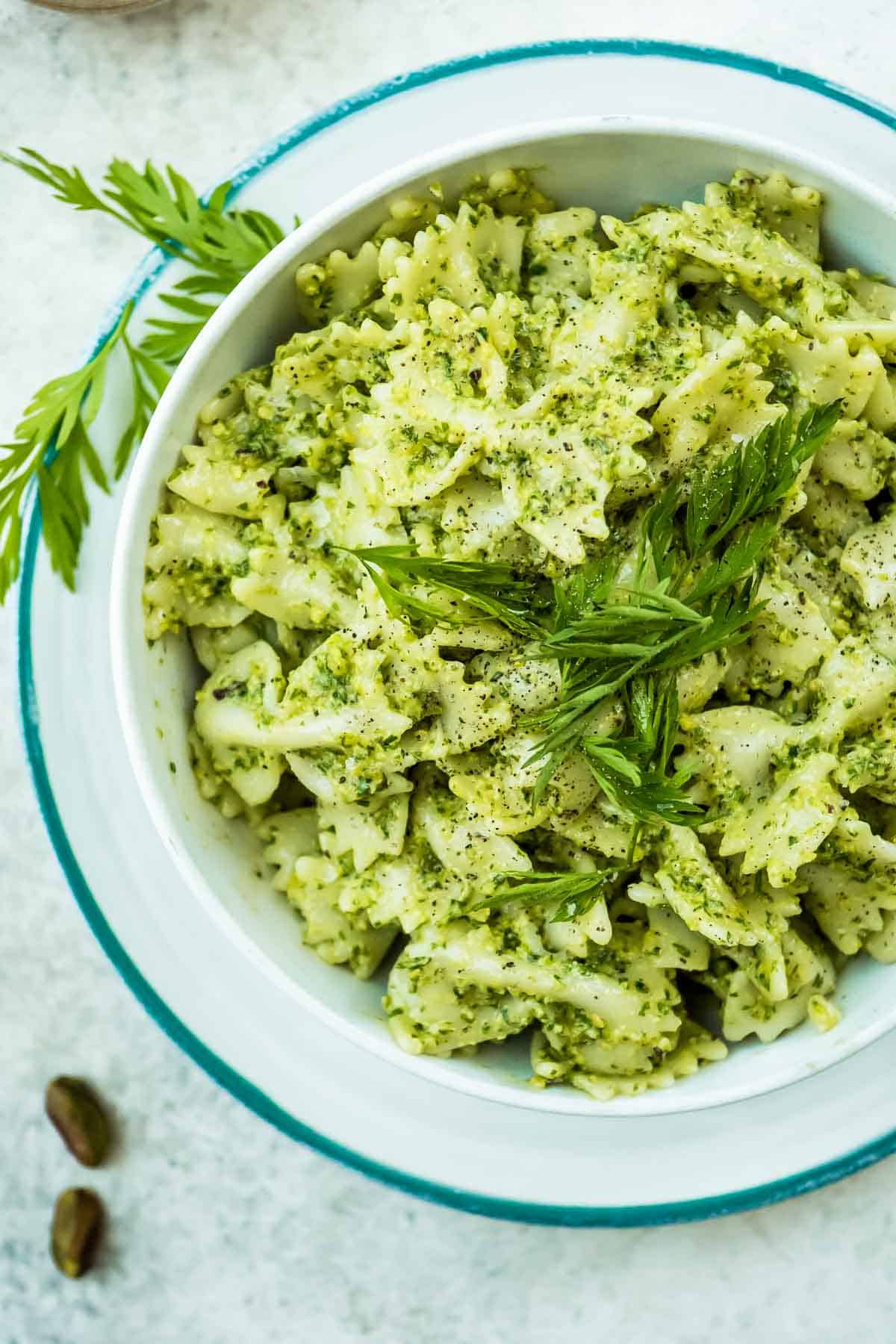 An overhead photo of bow tie pasta tossed with carrot top pesto in a bowl garnished with chopped carrot tops.