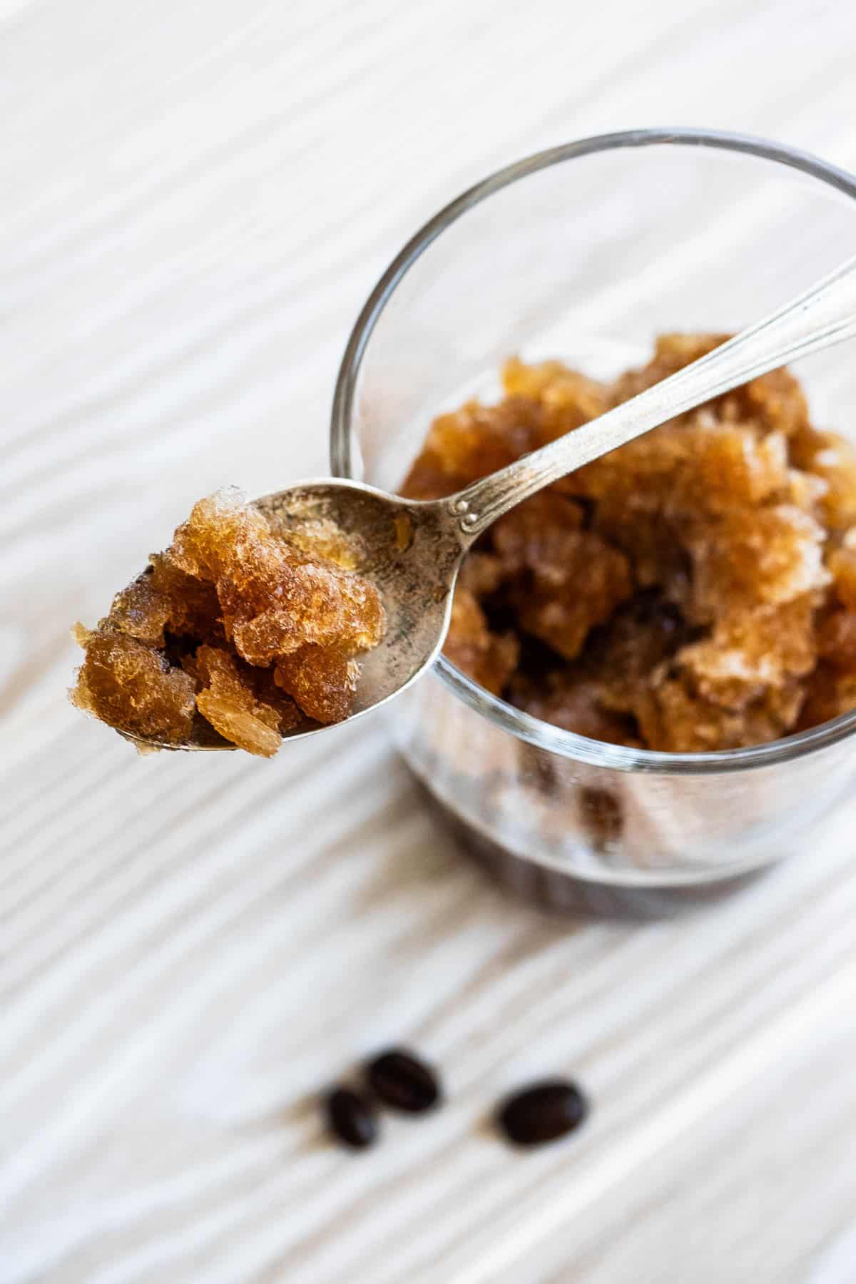 Coffee granita on a spoon being held over a glass of the granita.