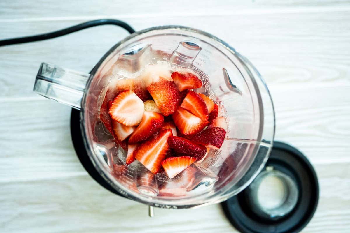 An overhead photo of strawberries, water and sugar in a blender.