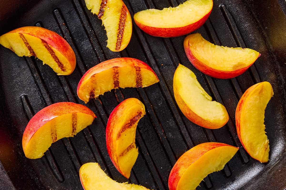 A close up of peach slices being grilled on a griddle.