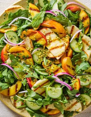 Halloumi and peach salad on a platter next to small bowls of chopped mint leaves and crushed pistachios.