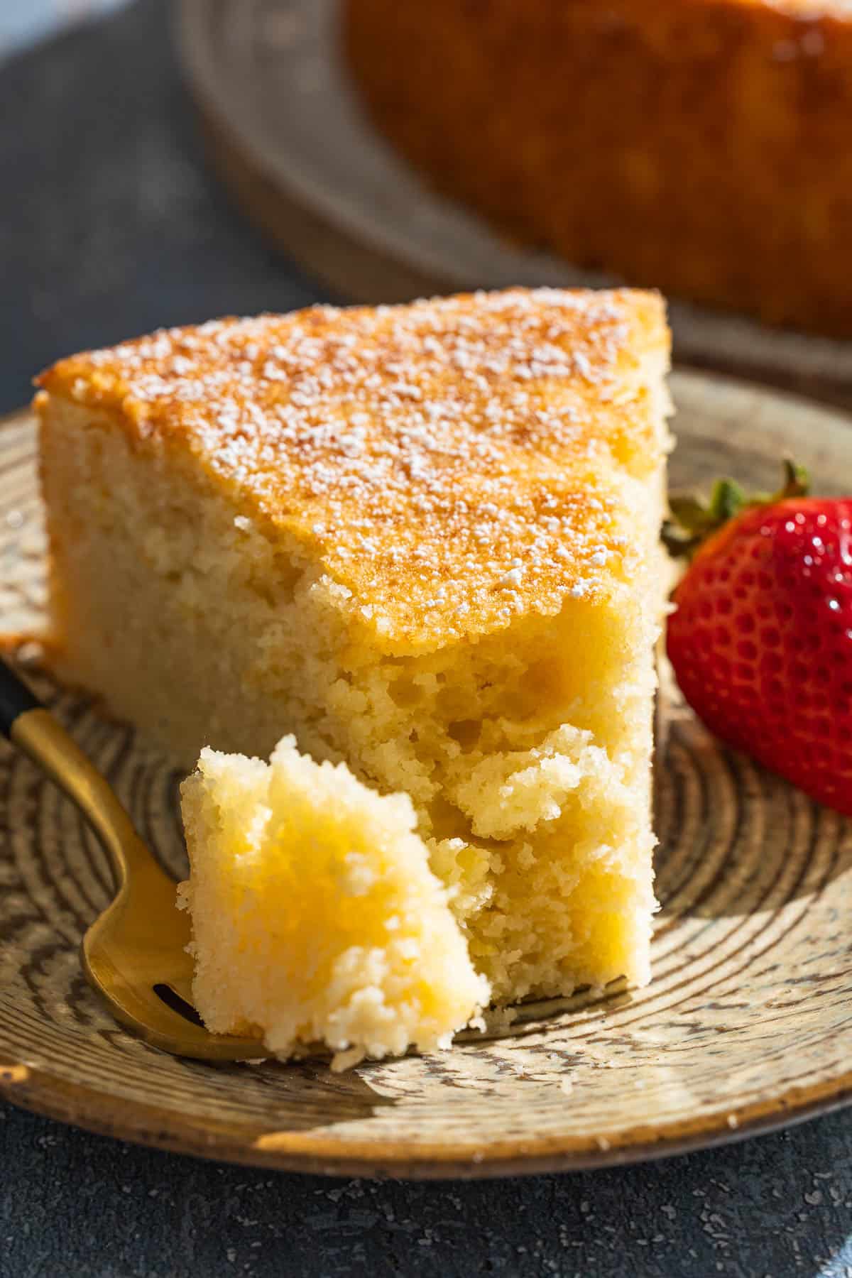 A close up of a slice of lemon ricotta cake on a plate with a strawberry and a fork.