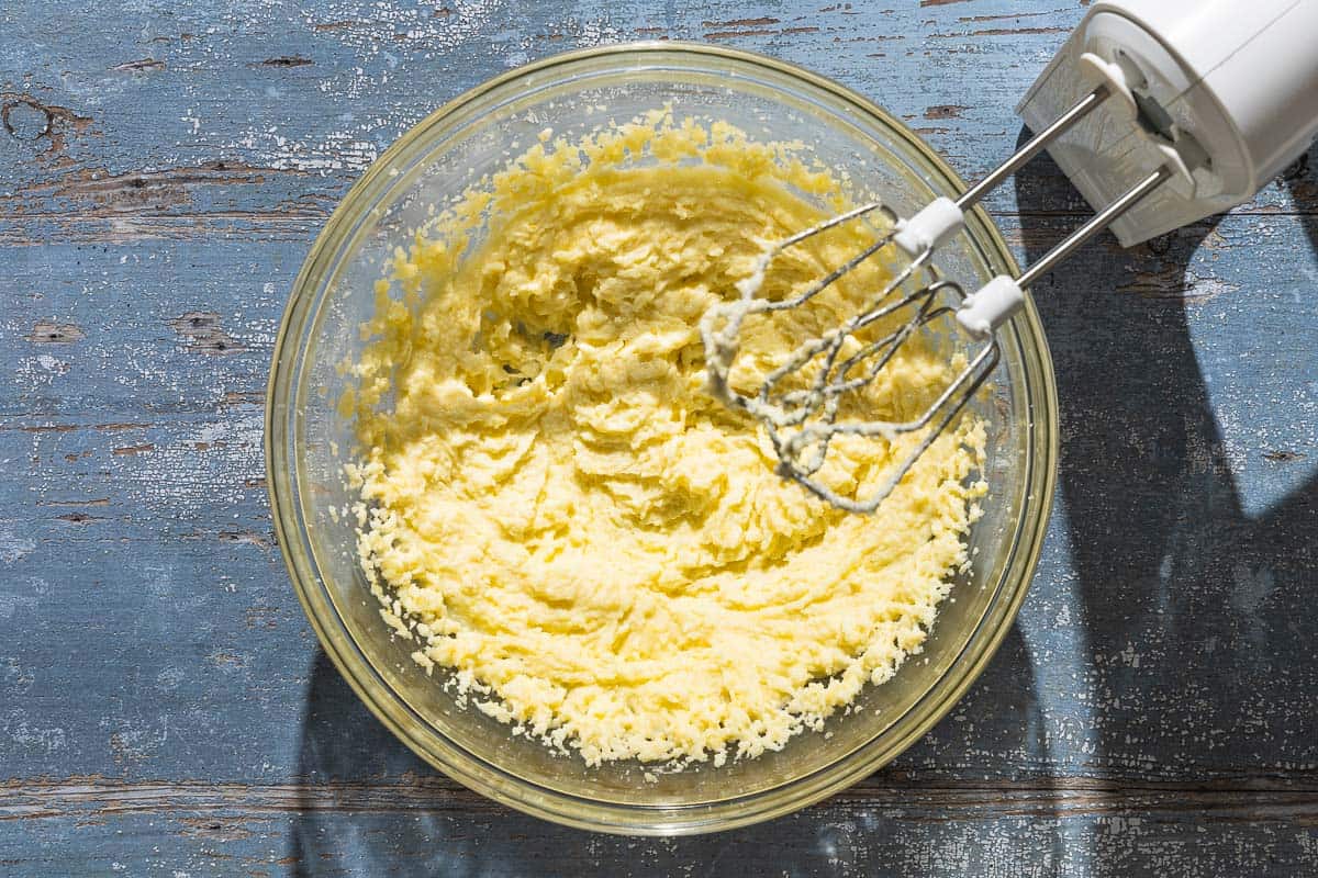 The ingredients for the lemon ricotta cake combined in a mixing bowl with a hand mixer.