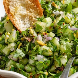A close up of a bowl of cucumber salsa with a toasted baguette slice and a spoon.