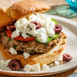 A close up of a greek style lamb burger on a plate.