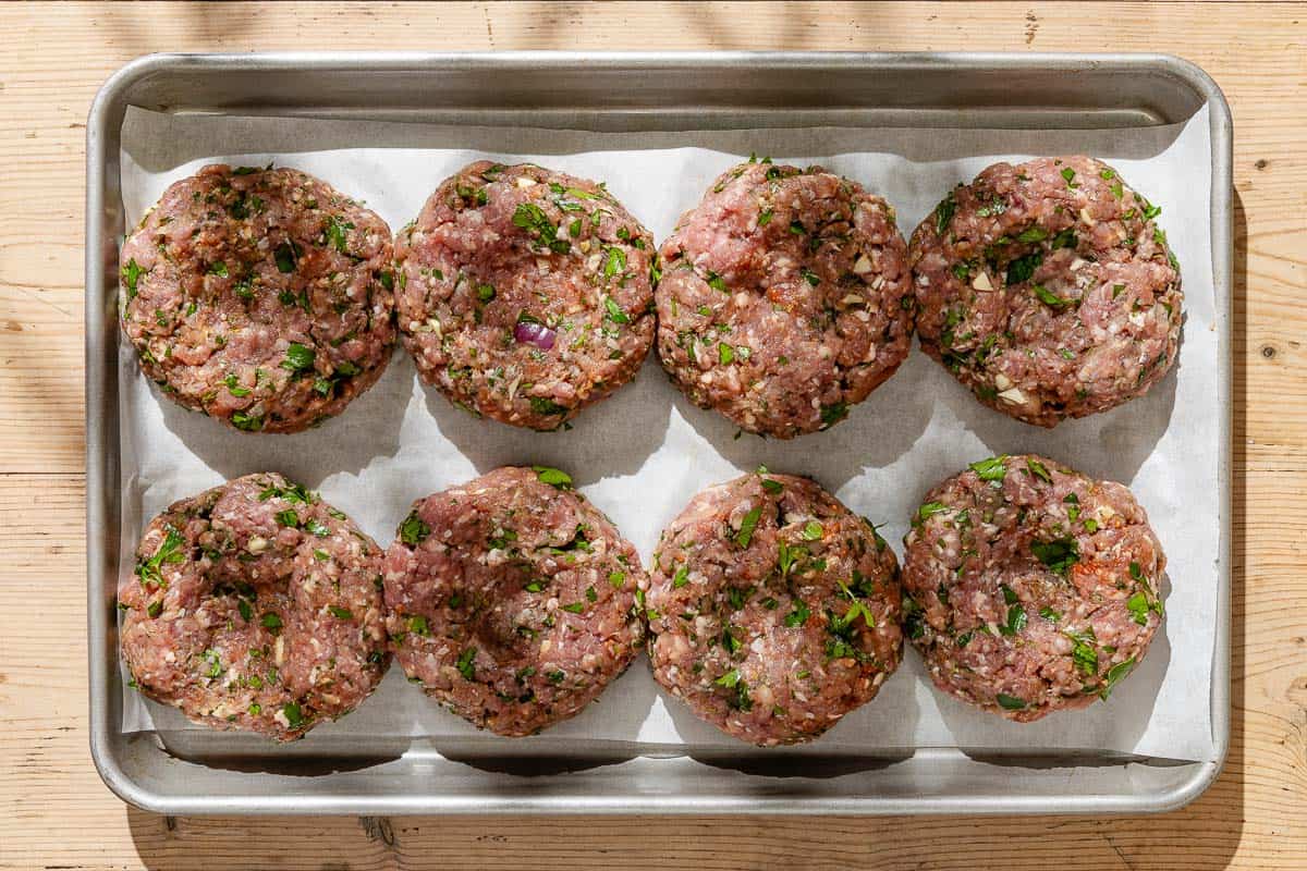An overhead photo of uncooked greek style lamb burger patties on a parchment lined baking sheet.