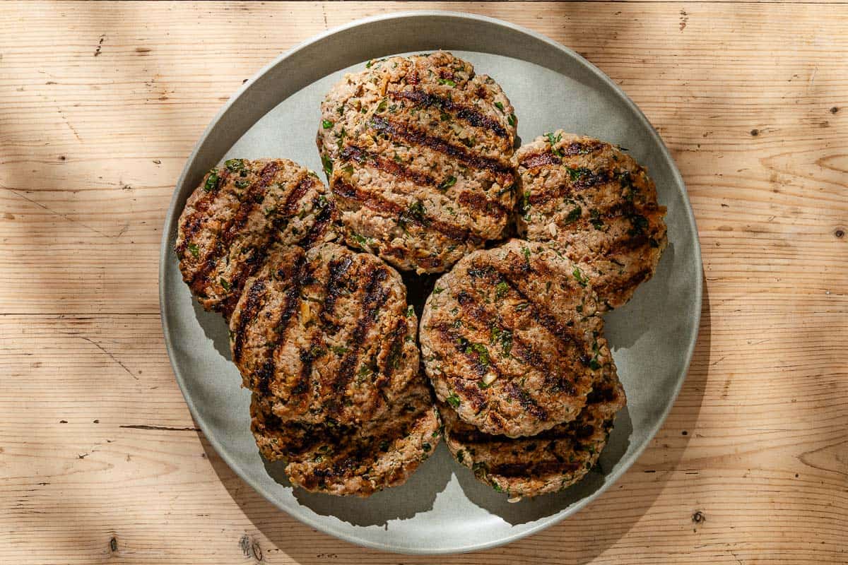 An overhead photo of grilled greek style lamb burger patties on a serving platter.
