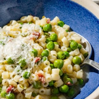 A close up of pasta with peas in a bowl with a spoon.