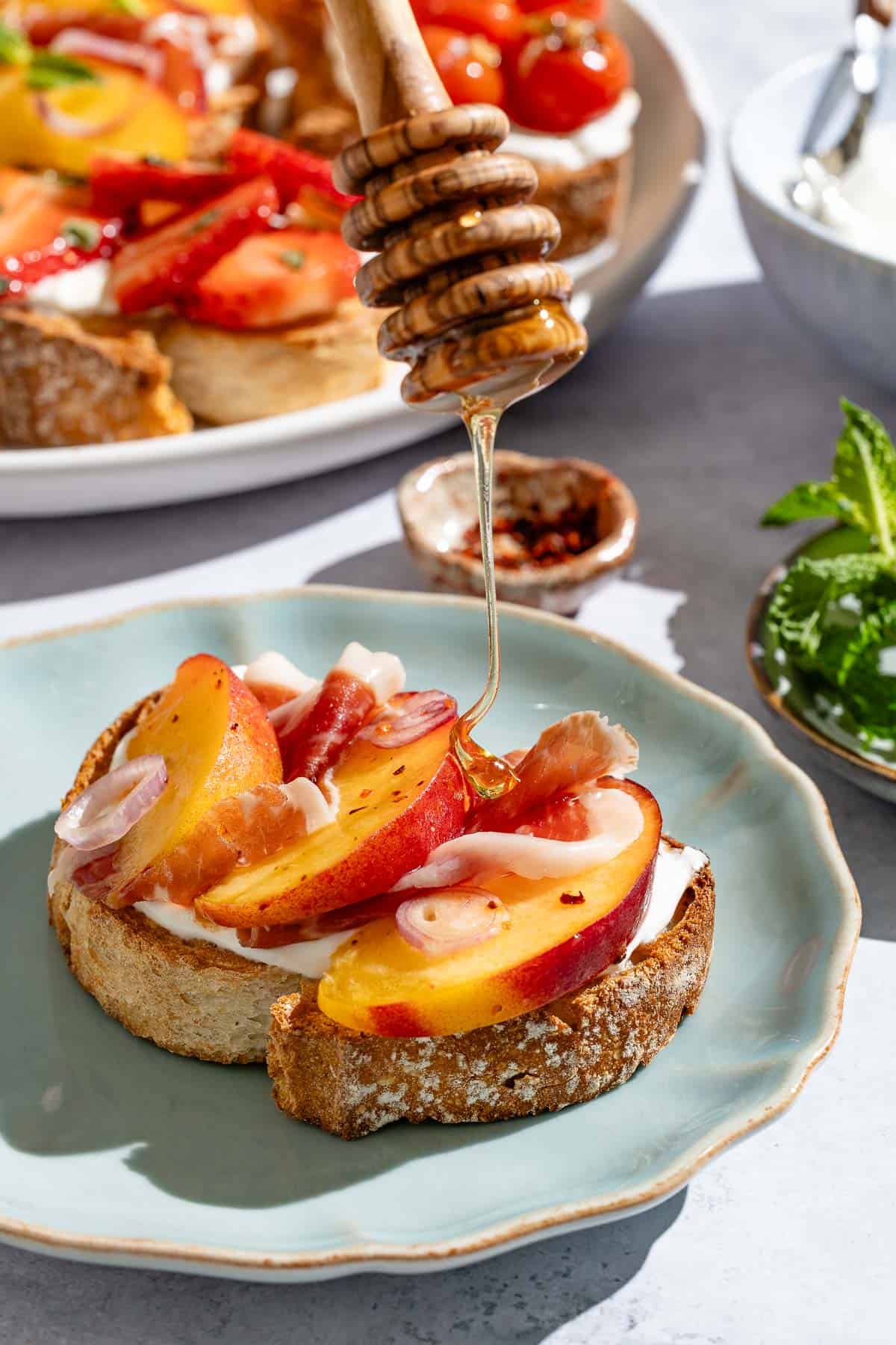 A close up of honey being drizzled on the prosciutto, peach and aleppo pepper ricotta toast.