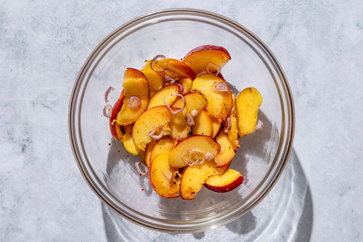 Sliced peaches in a bowl with sliced shallots and lemon juice.