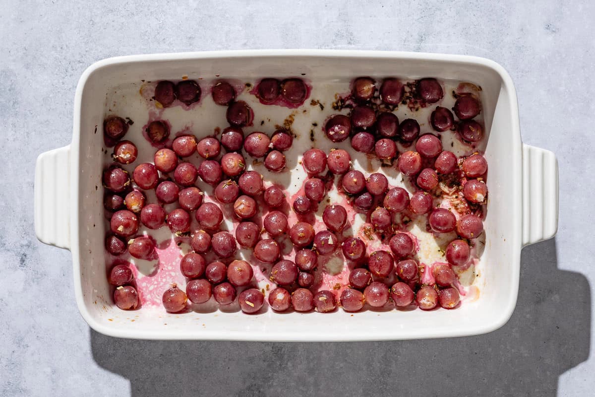 An overhead photo of roasted red grapes, fennel seed and rosemary in a baking dish.