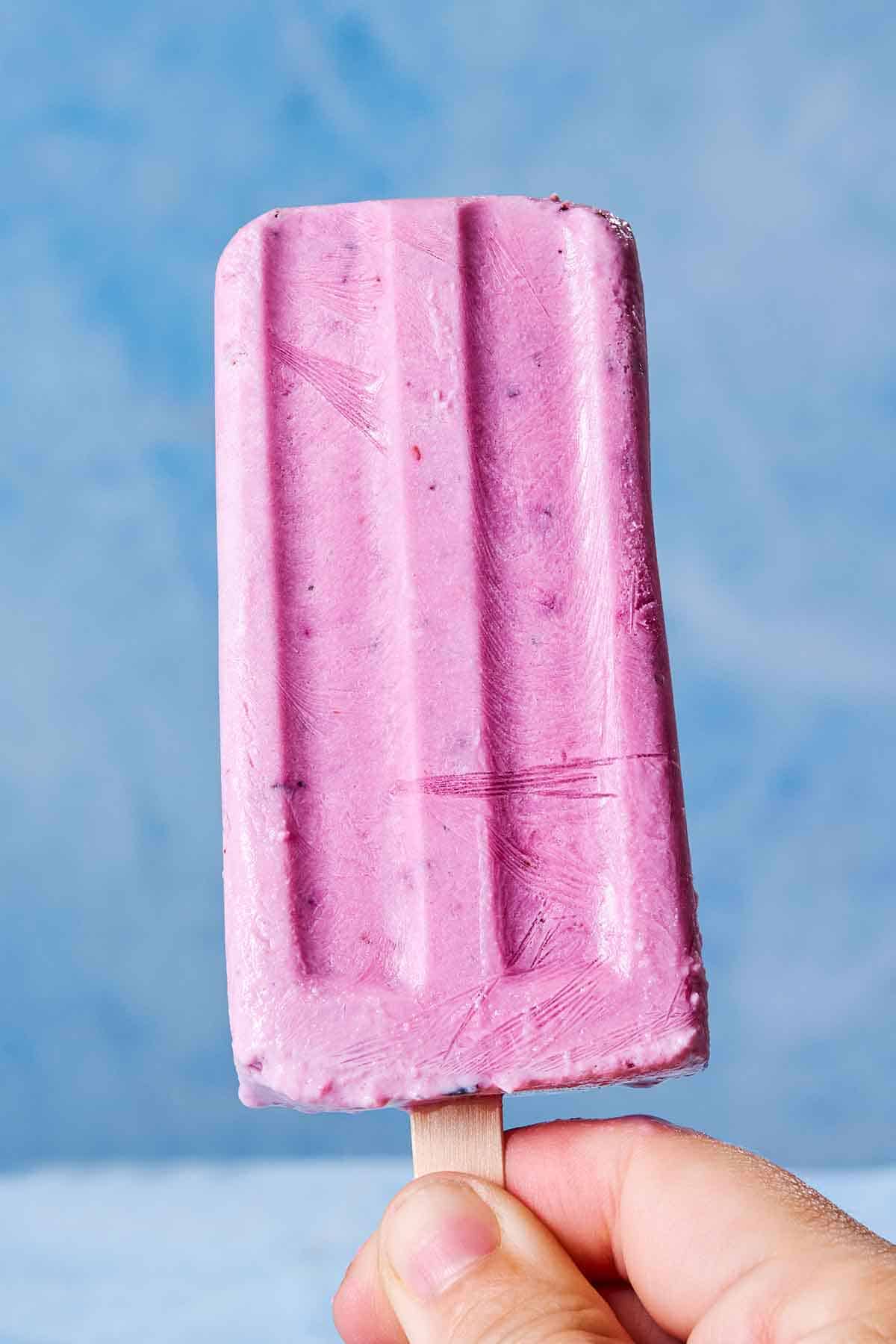 A close up of a hand holding a yogurt berry homemade popsicle.