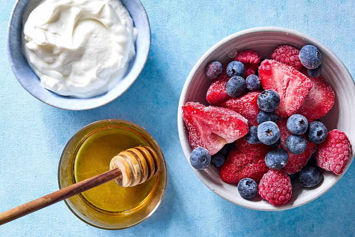 Ingredients for yogurt berry popsicles including greek yogurt, frozen mixed berries and honey.