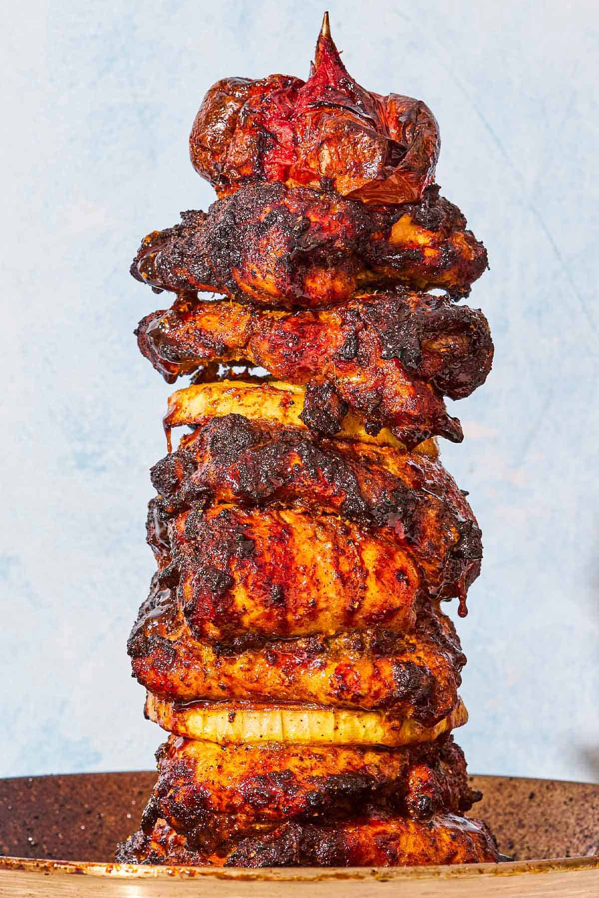 A close up of the grilled chicken shawarma on a vertical skewer with a tomato on top.