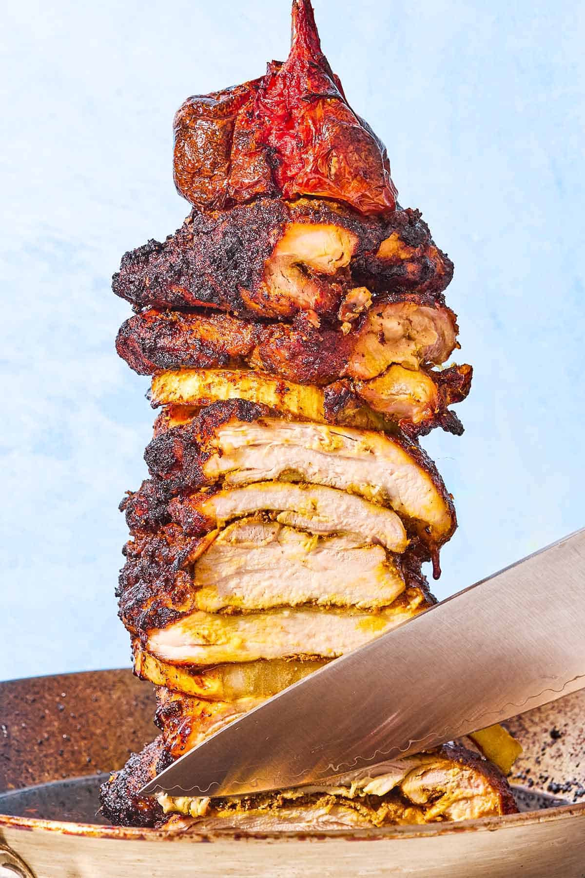 A knife cutting into the grilled chicken shawarma on a vertical skewer.