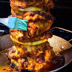 The grilled chicken shawarma on a vertical skewer being brushed with it's juices as it cooks on a grill.