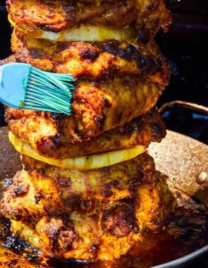 The grilled chicken shawarma on a vertical skewer being brushed with it's juices as it cooks on a grill.
