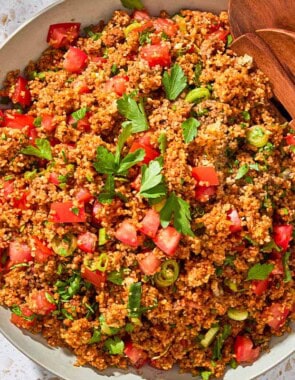 An overhead photo of kisir Turkish bulgur salad in a serving bowl with wooden serving utensils.