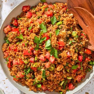 An overhead photo of kisir Turkish bulgur salad in a serving bowl with wooden serving utensils.