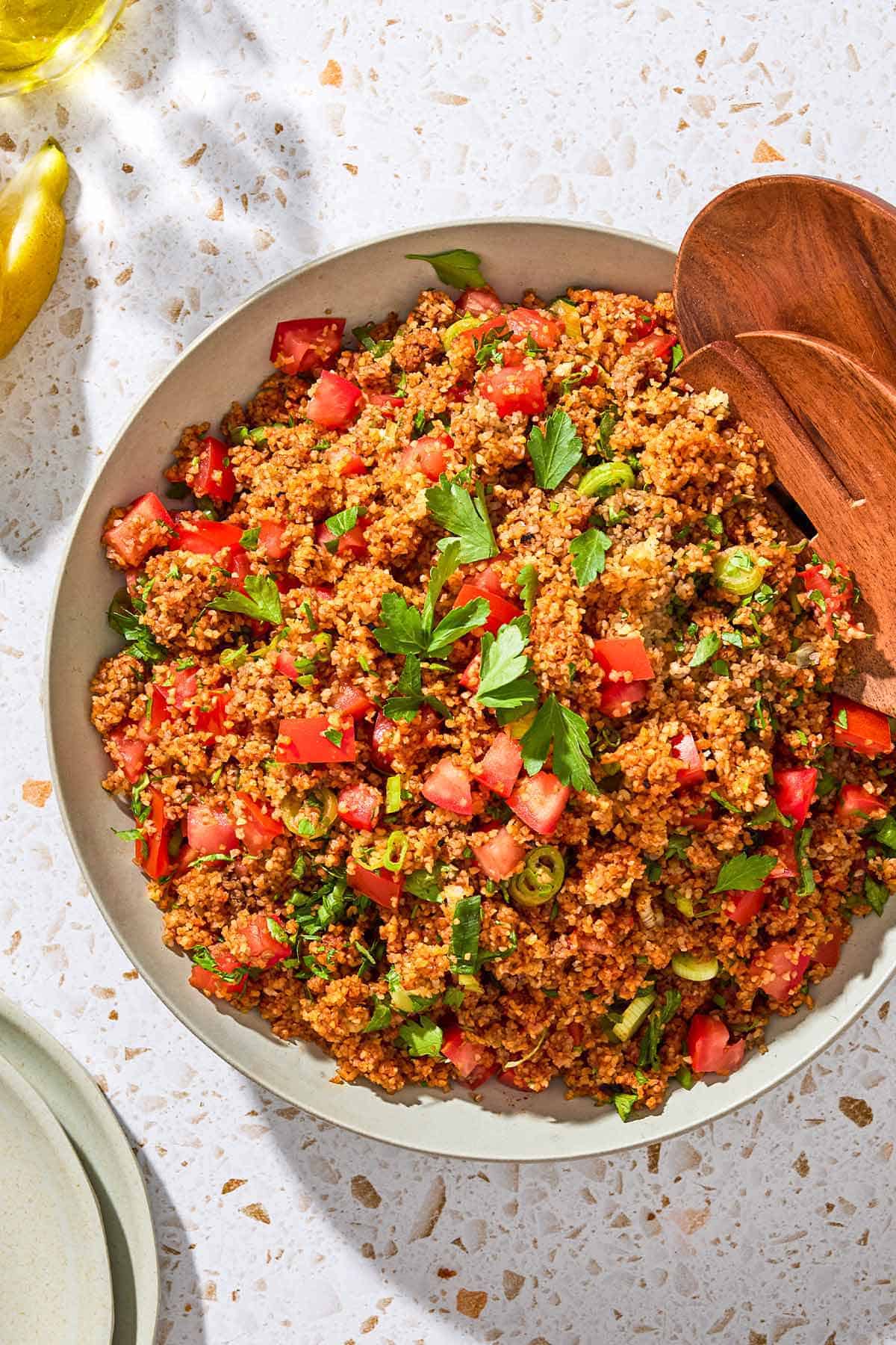 An overhead photo of kisir Turkish bulgur salad in a serving bowl with wooden serving utensils.