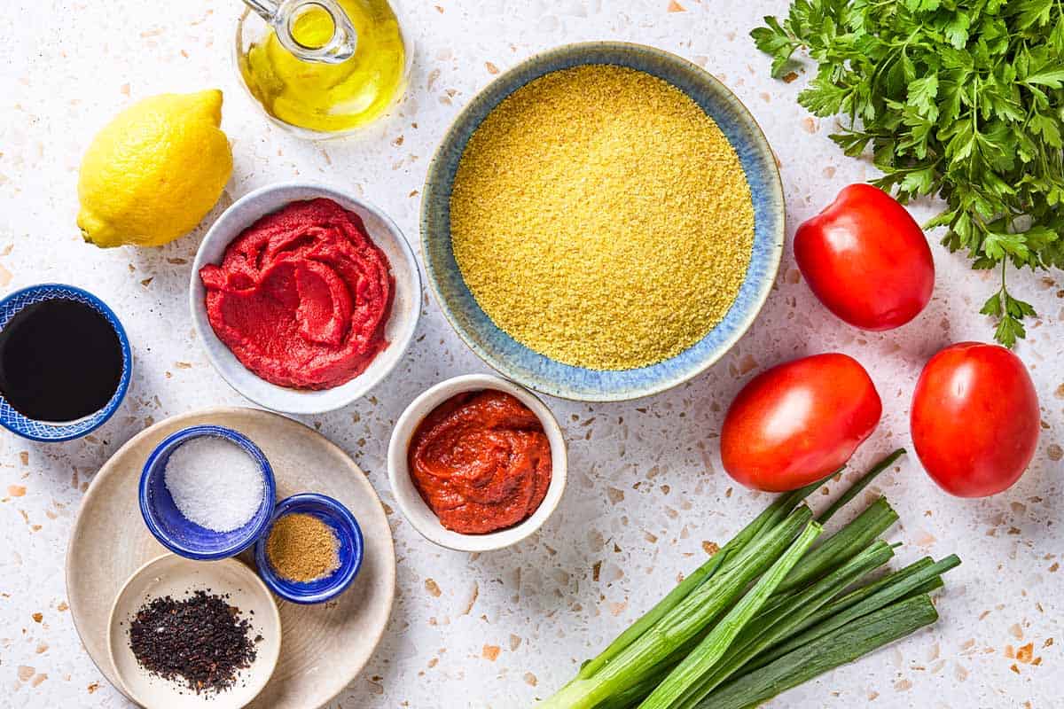 Ingredients for kisir turkish bulgur salad including extra fine bulgur, olive oil, tomato paste, Turkish red pepper paste, Urfa pepper, cumin, salt, pomegranate molasses, lemon, green onions, roma tomatoes, and parsley.