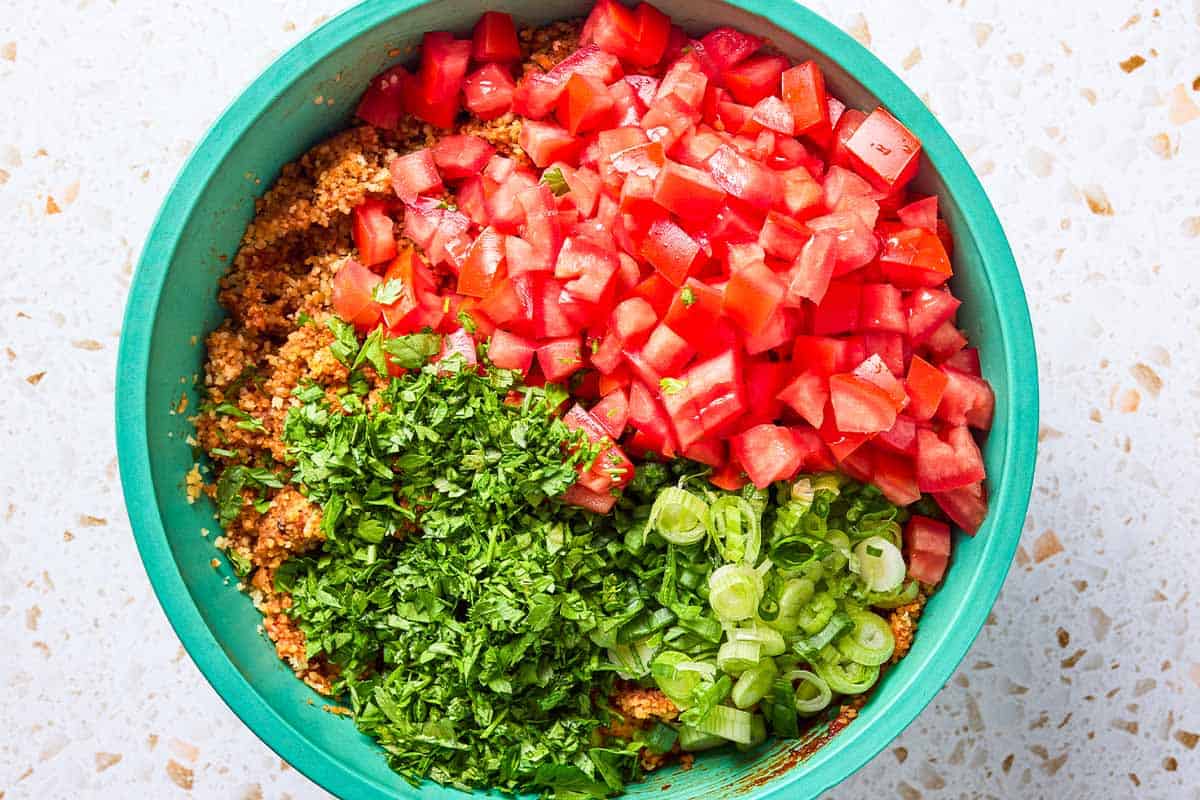 An overhead photo of the prepared bulgur and chopped green onions, tomatoes and parsley in a bowl just before being mixed together.