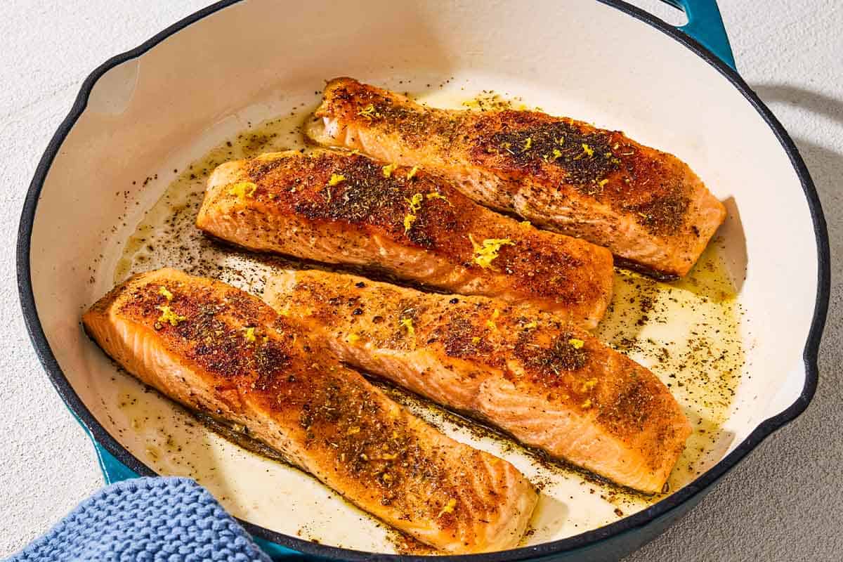 A close up of 4 pan seared salmon filets in a skillet.