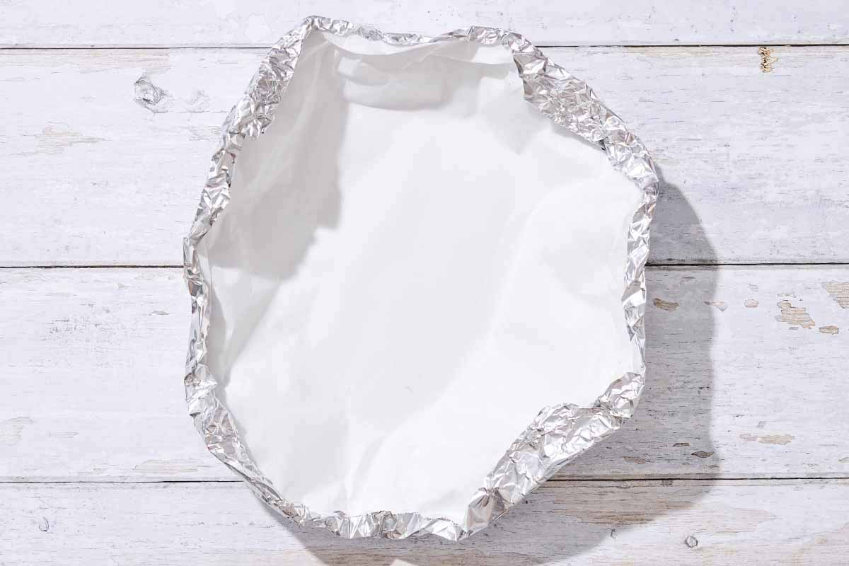 A sheet of foil lined with parchment paper and formed into a bowl-like shape.