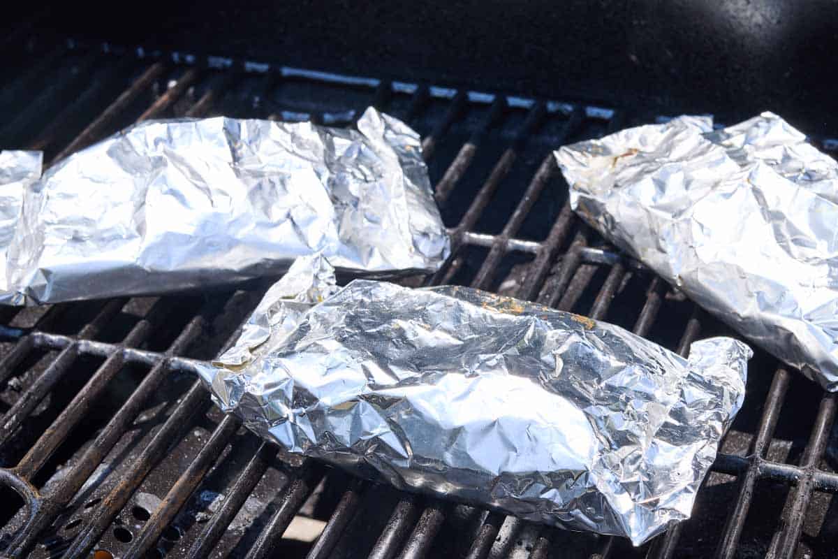 3 sealed grilled shrimp packets on a grill.