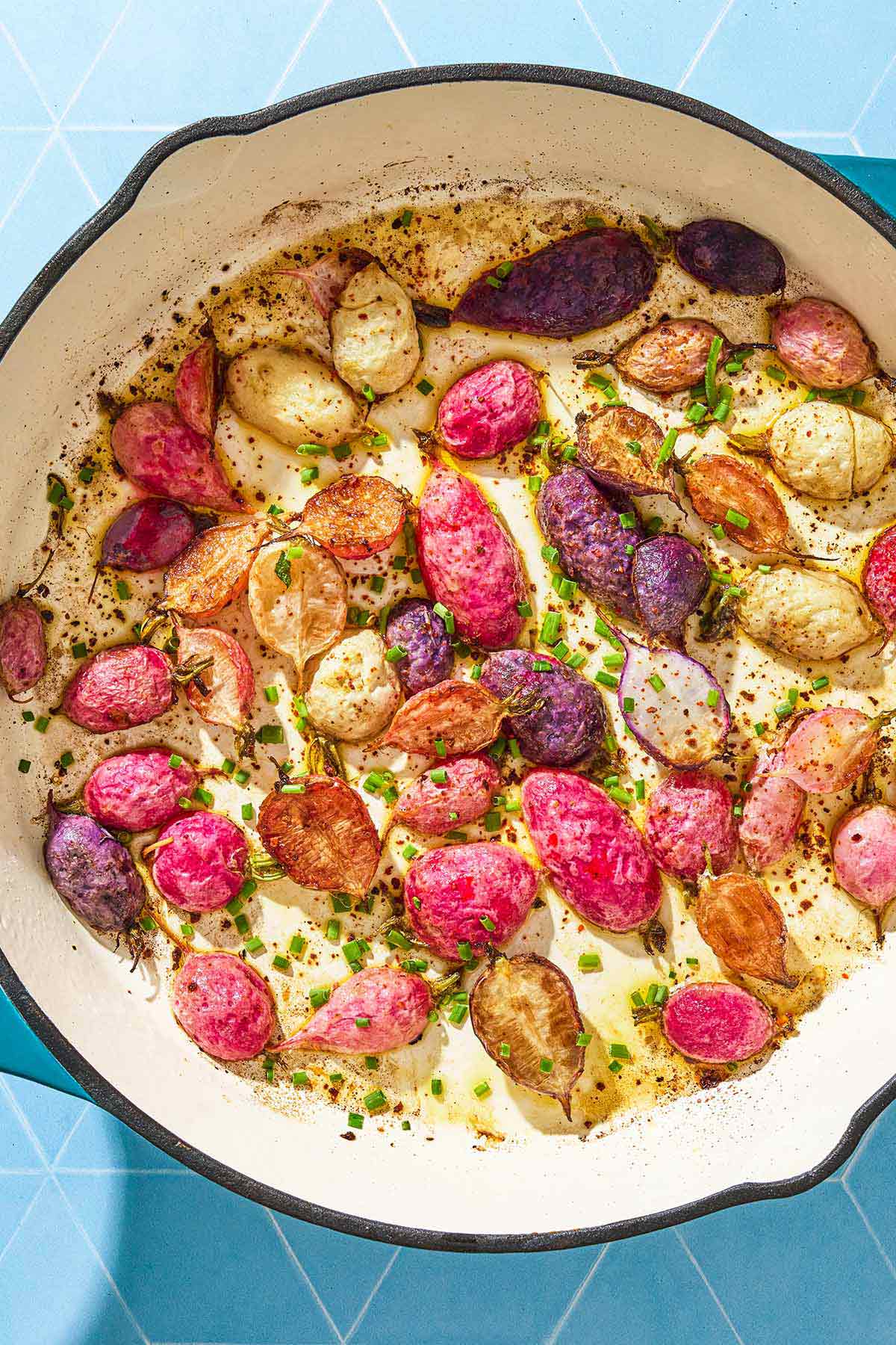 An overhead photo of roasted radishes in a skillet garnished with chives.