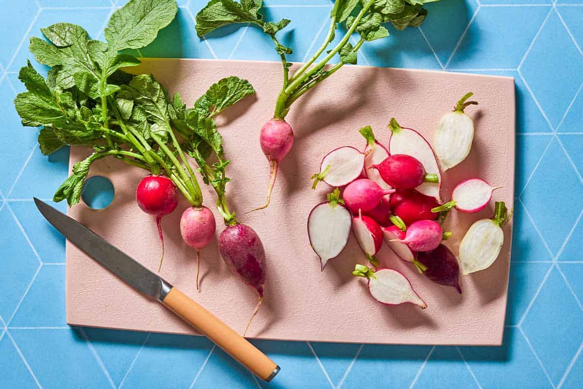 Whole radishes and a handful of halved radishes on a cutting board with a knife.