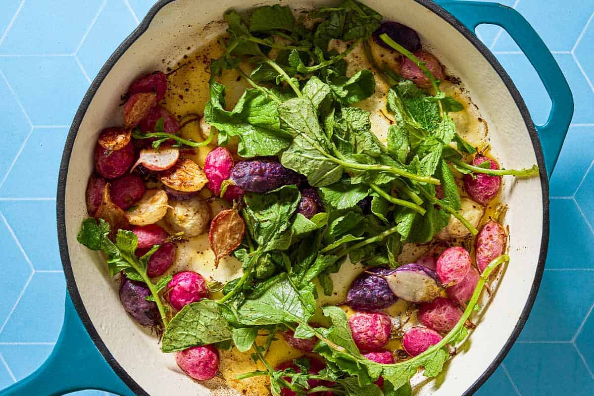An overhead photo of roasted radishes with their greens in a skillet.