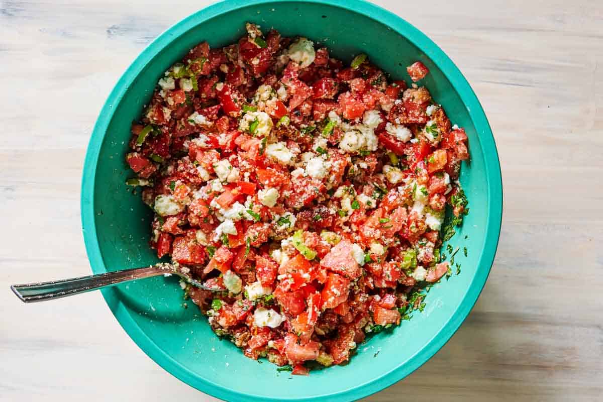 The ingredients for greek tomato fritters in a bowl with a spoon just after being mixed together.