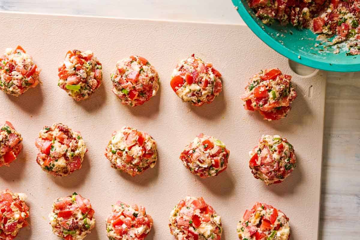 An overhead photo of uncooked tomato fritters on a cutting board next a bowl of the fritter mix.