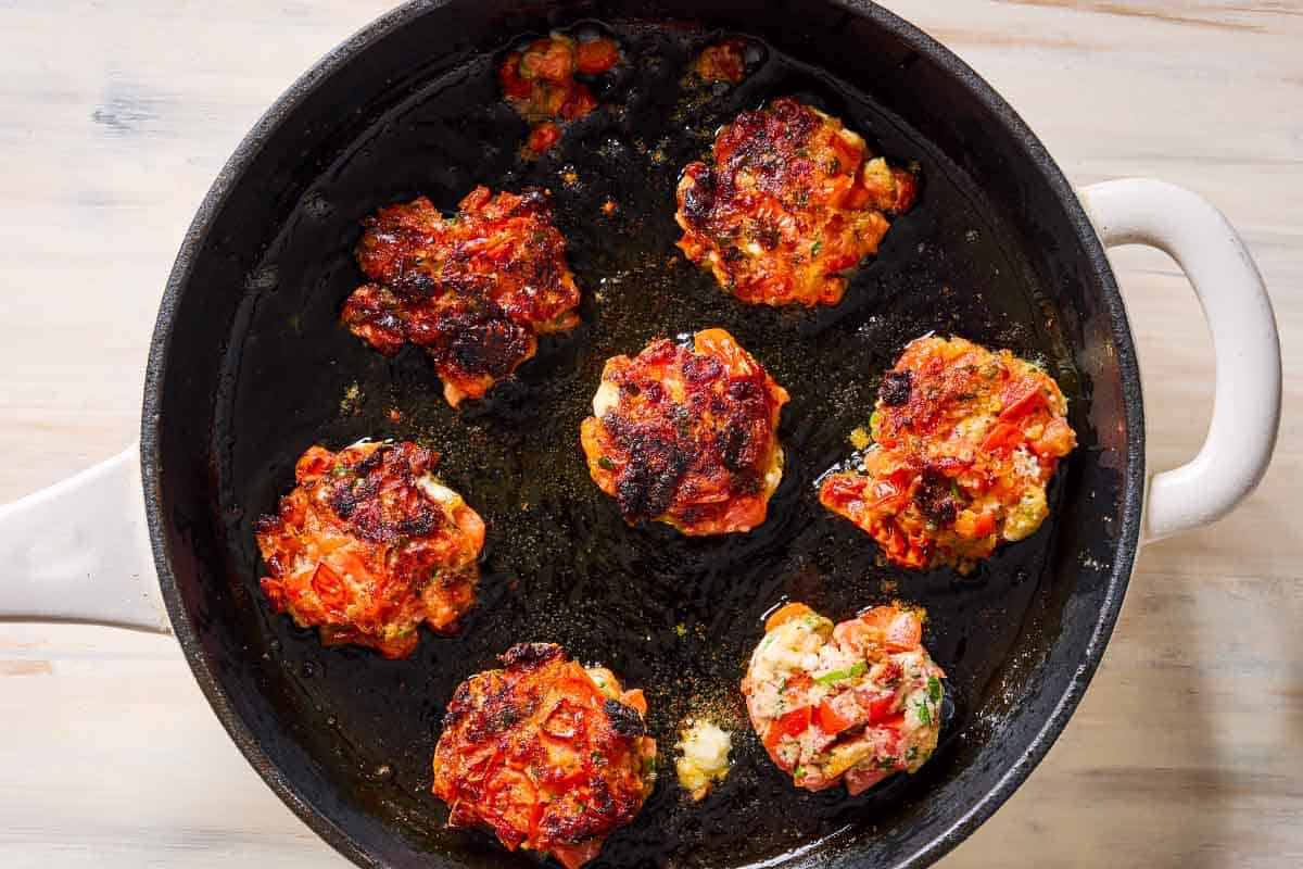 7 tomato fritters being fried in a skillet.