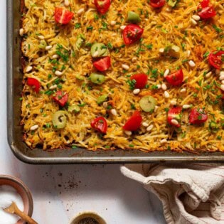 Baked hash browns on a sheet pan next to a kitchen towel and bowls of salt and pepper.