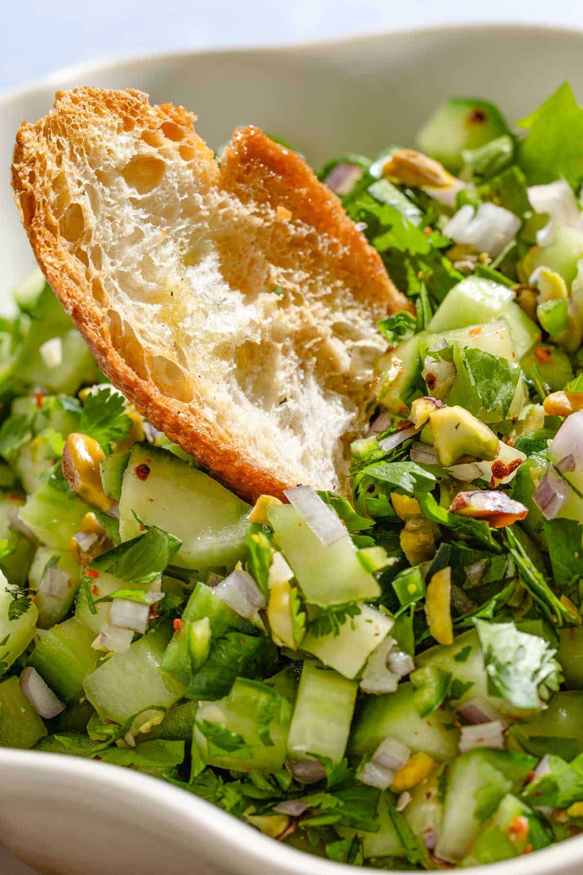A close up of a bowl of cucumber salsa with a toasted baguette slice.