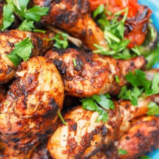 A close up of grilled chicken drumsticks garnished with parsley on a serving platter.