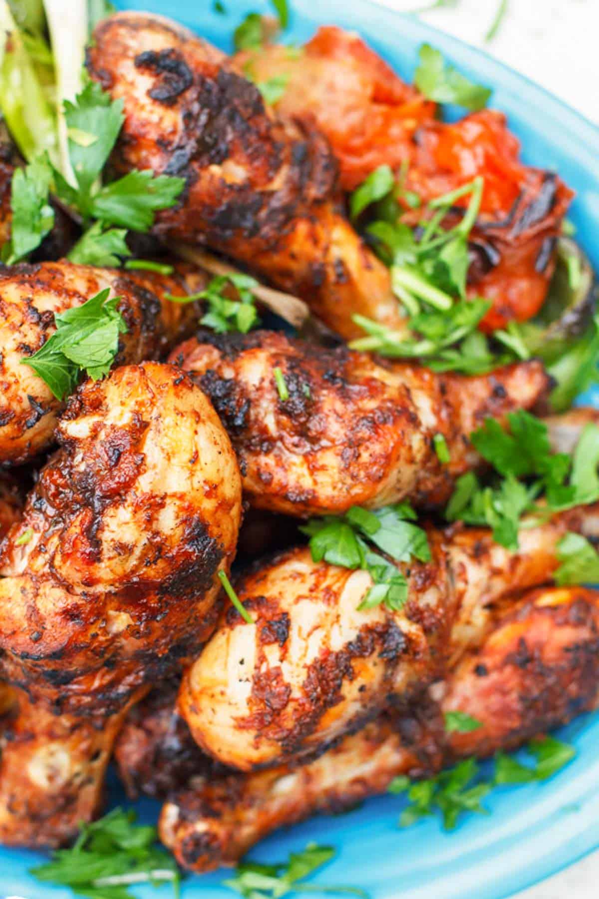 A close up of grilled chicken drumsticks garnished with parsley on a serving platter.