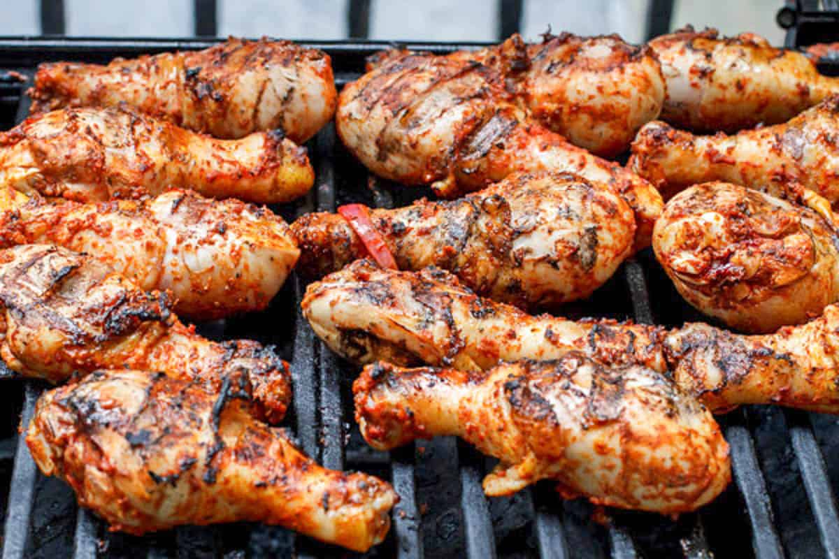 Marinated chicken drumsticks being grilled on a gas grill.