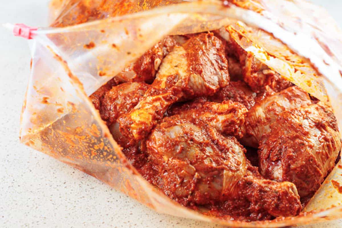 Chicken drumsticks being marinaded in a large zip top plastic bag.