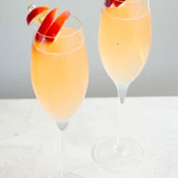 A close up of 2 peach bellinis garnished with peach slices.