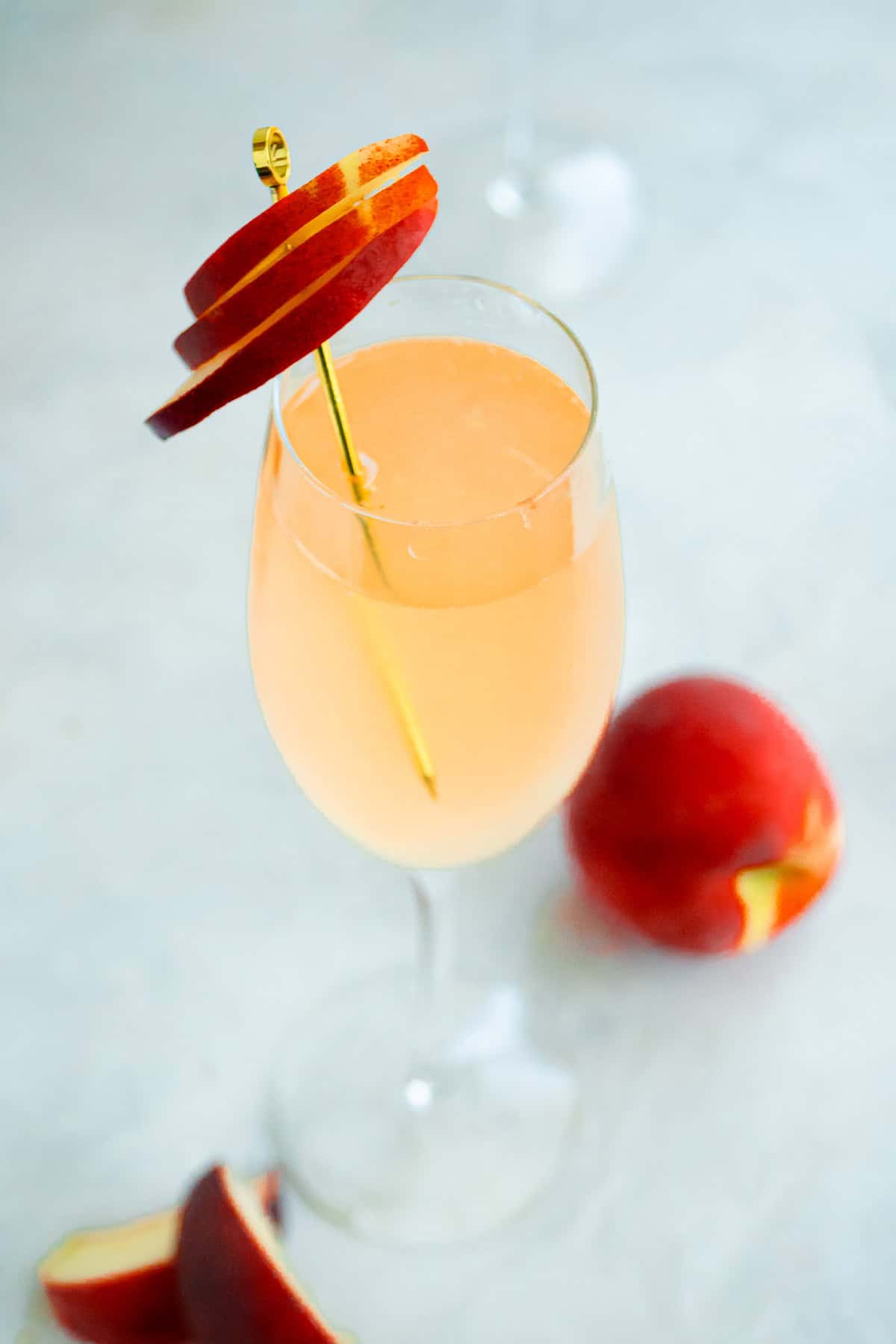 A close up of a peach bellini garnished with peach slices, with more peaches in the background.