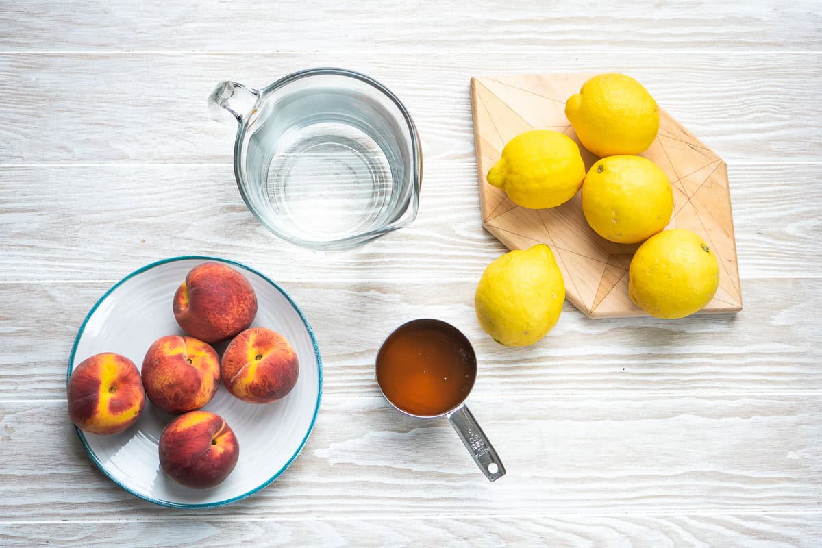 Ingredients for peach lemonade including lemons, honey, water and peaches.