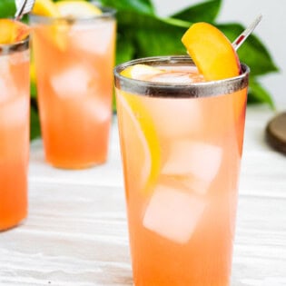A close up of a glass of peach lemonade in front of 2 more glasses of the lemonade.